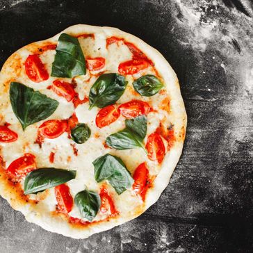 Mozarella pizza på svart flate med mel rundt