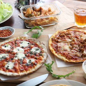 To pizzaer på et bord med drikke, salat og dressinger