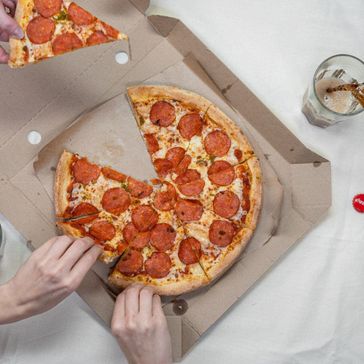 Pizza som blir tatt fra papp-emballasje og cola servert ved siden av